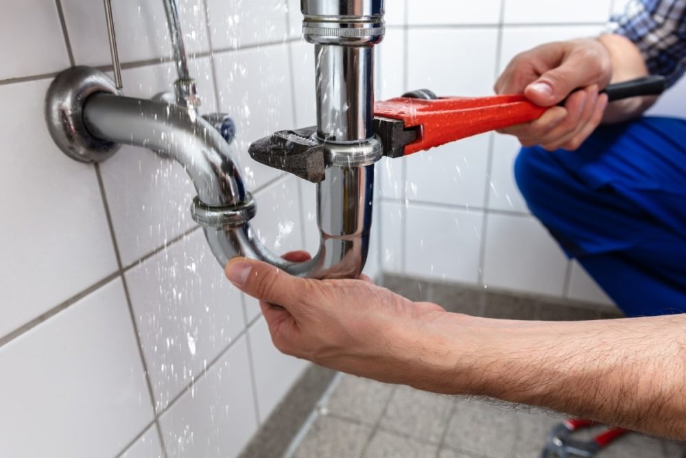 Close-up of hands using a wrench on a spraying pipe, illustrating a tenant's responsibility in addressing maintenance issues promptly.