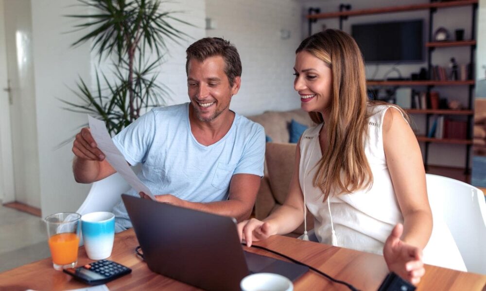 Couple looking at a laptop screen and paper with a calculator on the table.