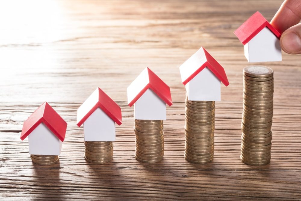 Stacked coins with small house models on top, representing investment growth and answering the question what does a property manager do to maximise rental income.