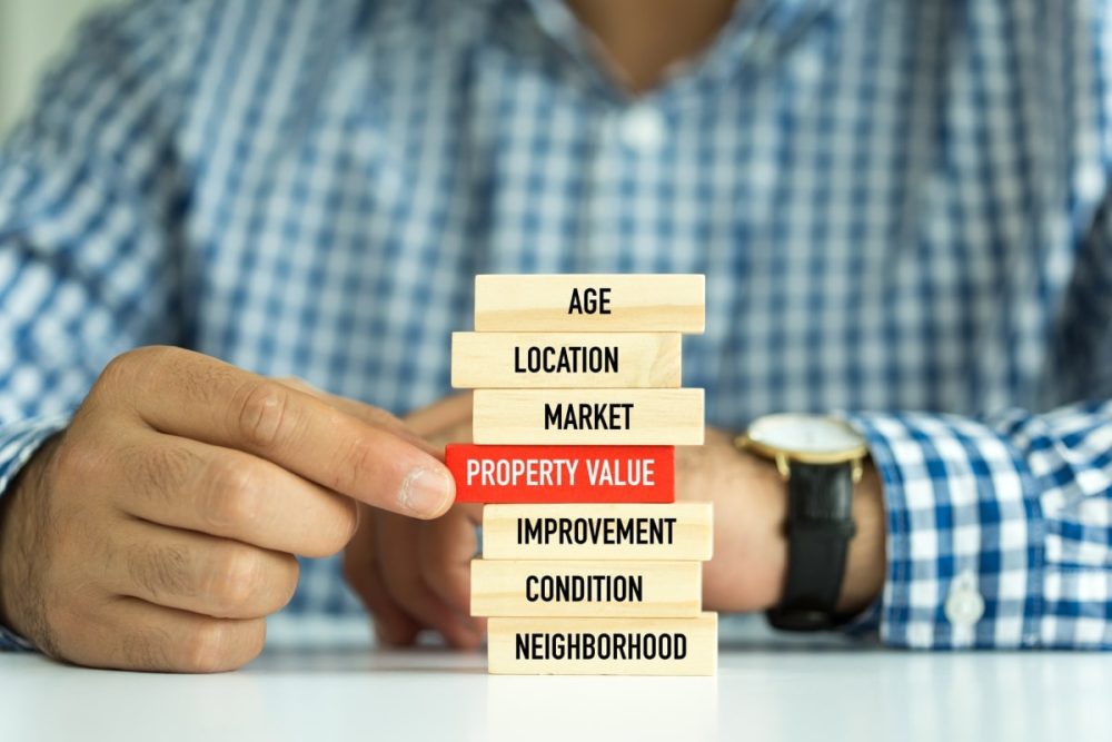 Man pulling out a wooden block stating "PROPERTY VALUE" from a jenga tower.