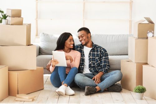 Two young adults, amid moving boxes in their new living space, demonstrate the excitement and positive attitude that are indicative of a good tenant's qualities.