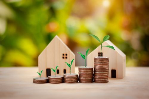 Stacked coins increasing in height next to two wooden house models, symbolising the financial planning needed for buying a second home.